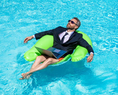 Mann entspannt im Pool im Anzug in einem Schwimmreifen, mit Laptop auf dem Schoß