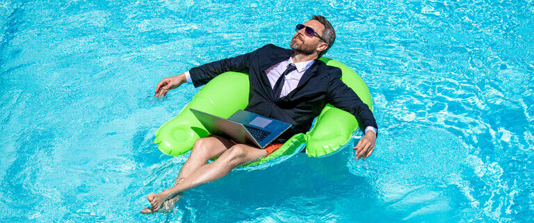 Mann entspannt im Pool im Anzug in einem Schwimmreifen, mit Laptop auf dem Schoß