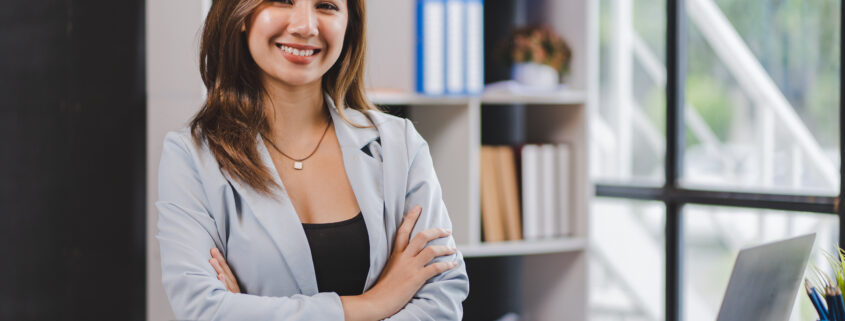 Lächelnde asiatische Geschäftsfrau, die im modernen Büro am Laptop arbeitet