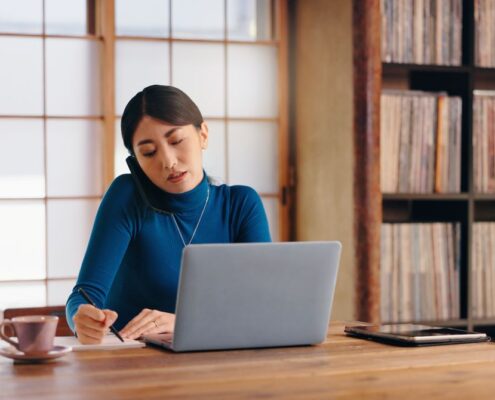 Frau am Schreibtisch mit Laptop und Notizblock – konzentrierte Textarbeit für das Buch Lektorat in gemütlicher Umgebung.