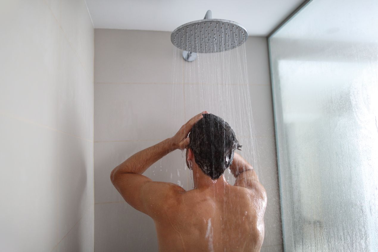 Duschrückwand hinter Regendusche, Mann beim Haarewaschen in modernem Bad mit Glasabtrennung