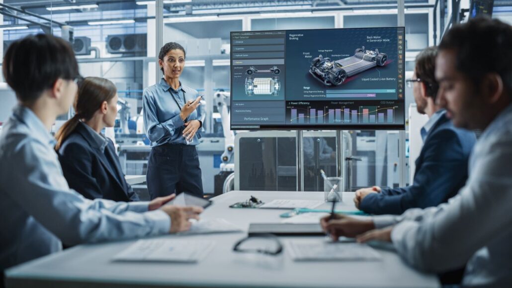 Ingenieurin praesentiert Team ein APS System mit digitalen Echtzeitdaten und 3D Modell zur Planung effizienter Produktionsablaeufe