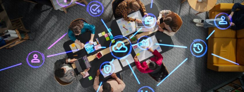 Team arbeitet gemeinsam an digitalen Projekten, vernetzt durch ein APS System mit Symbolen fuer Kommunikation und Effizienz